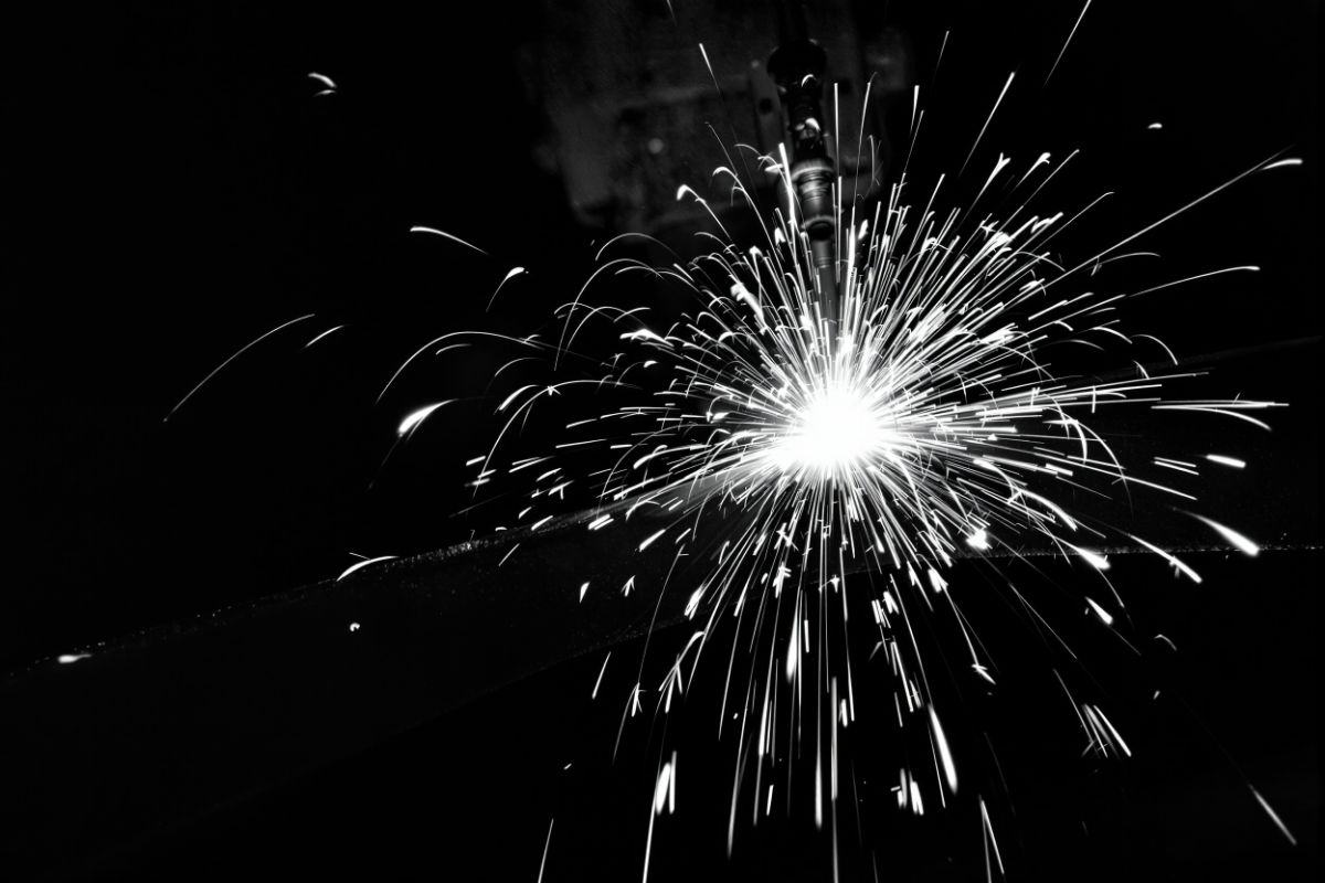 Arc welding in a dark workshop: a fountain of sparks leaves the weld point on a steel beam.